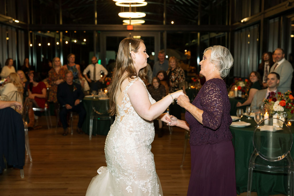 Bride dancing with a family member during the reception, surrounded by guests in a warmly lit indoor space.