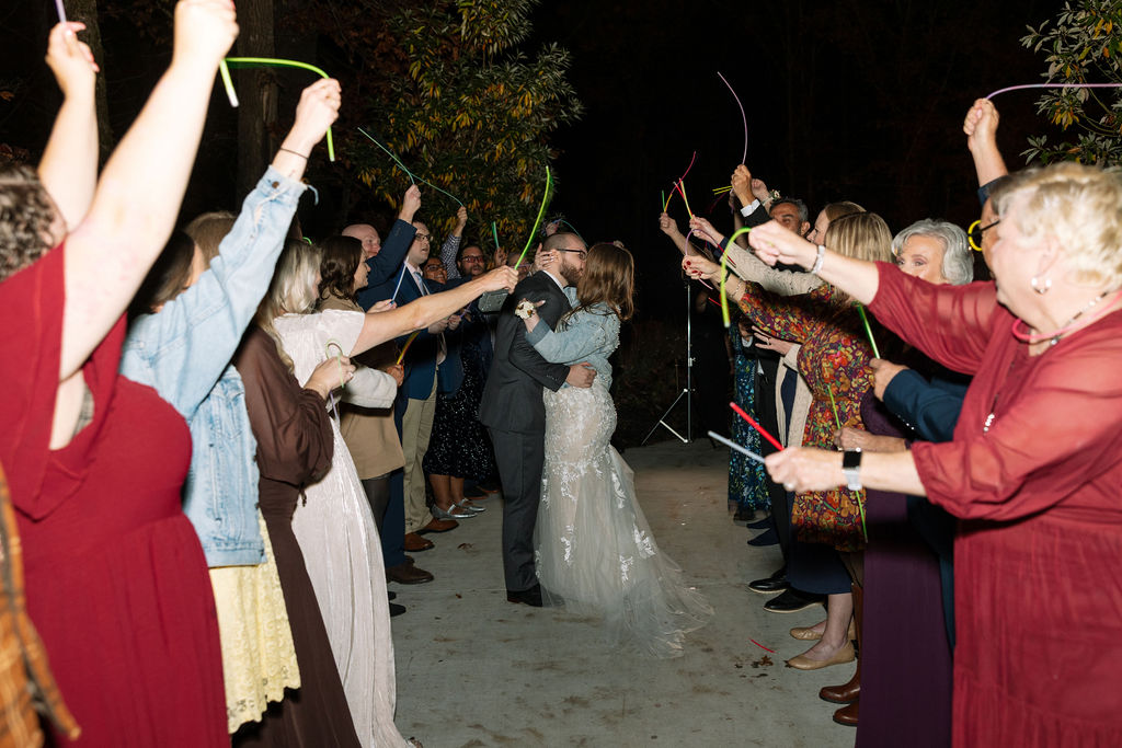 Wedding guests cheering during a glow stick exit at a Smoky Mountain wedding venue, celebrating the couple at night.