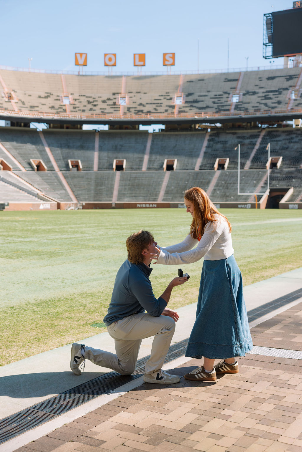Couple celebrating surprise proposal on Neyland Stadium field with University of Tennessee backdrop