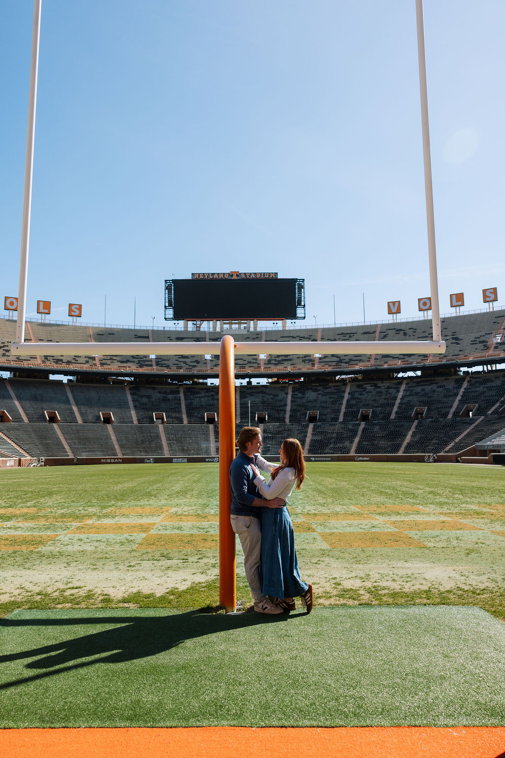 Engaged couple standing beneath Neyland Stadium goalpost after surprise proposal in Knoxville