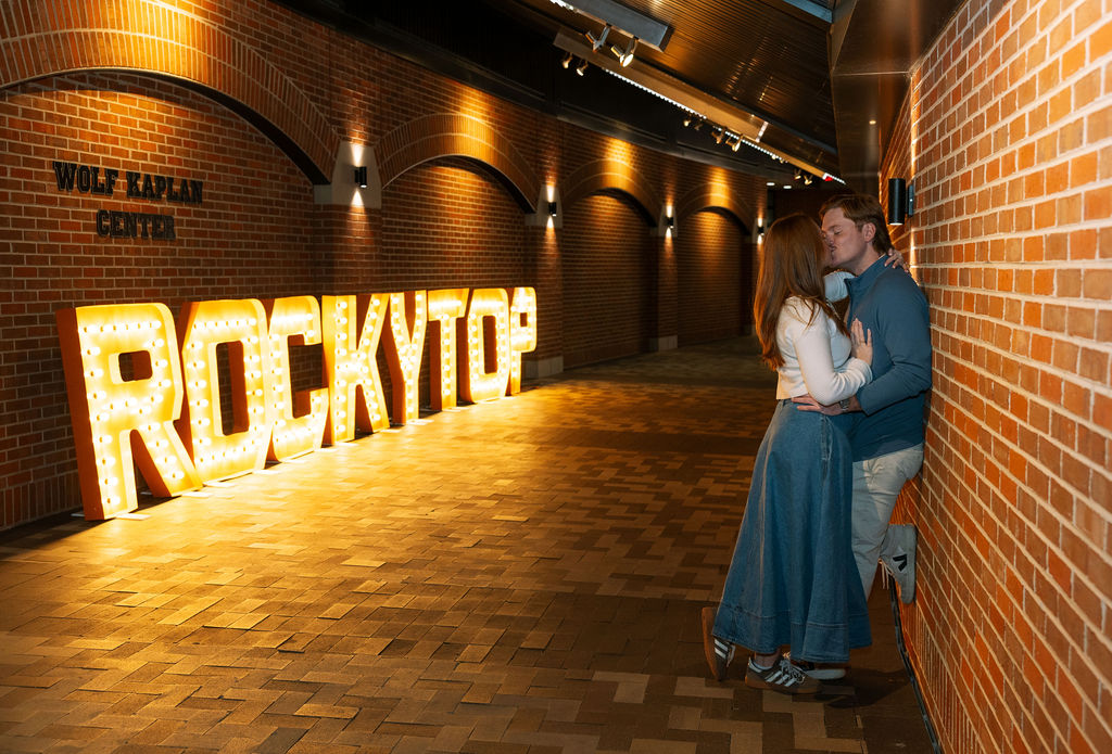 Couple embracing beside Rocky Top sign inside Neyland Stadium after Knoxville proposal