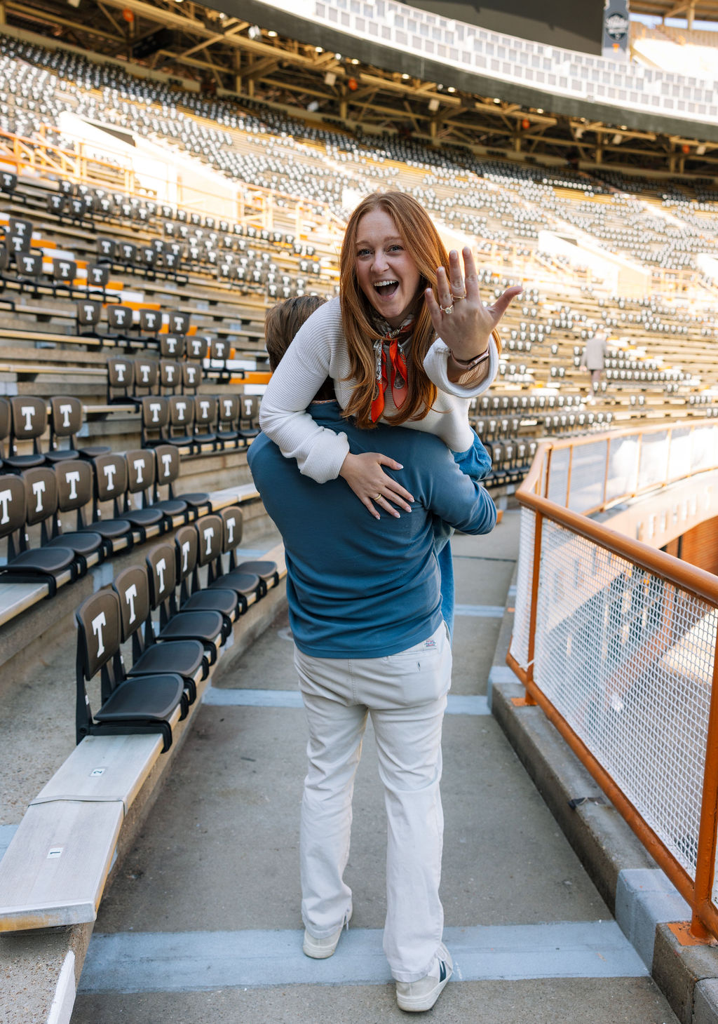 Woman showing engagement ring while celebrating surprise proposal inside Neyland Stadium stands