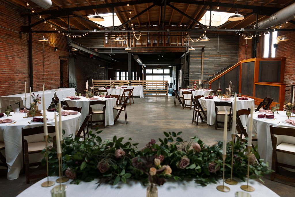 Industrial wedding reception space with round tables, candles, and soft overhead lighting