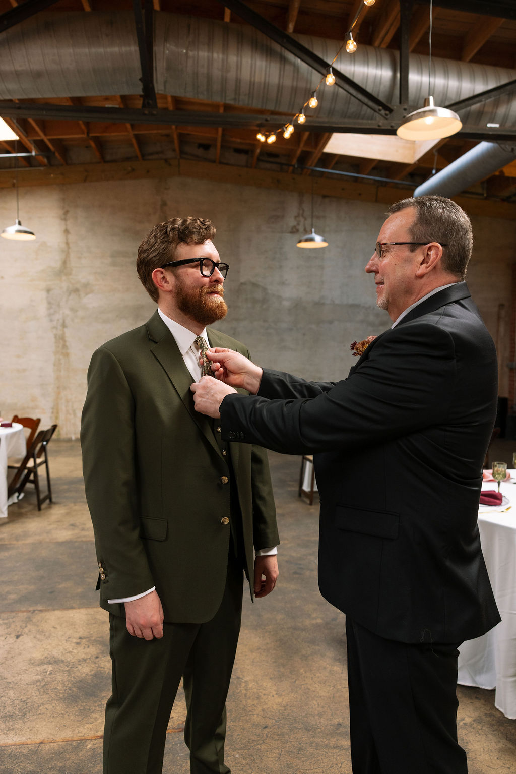Groom having his tie adjusted by a family member inside an industrial wedding venue, photographed by a wedding photographer in Knoxville