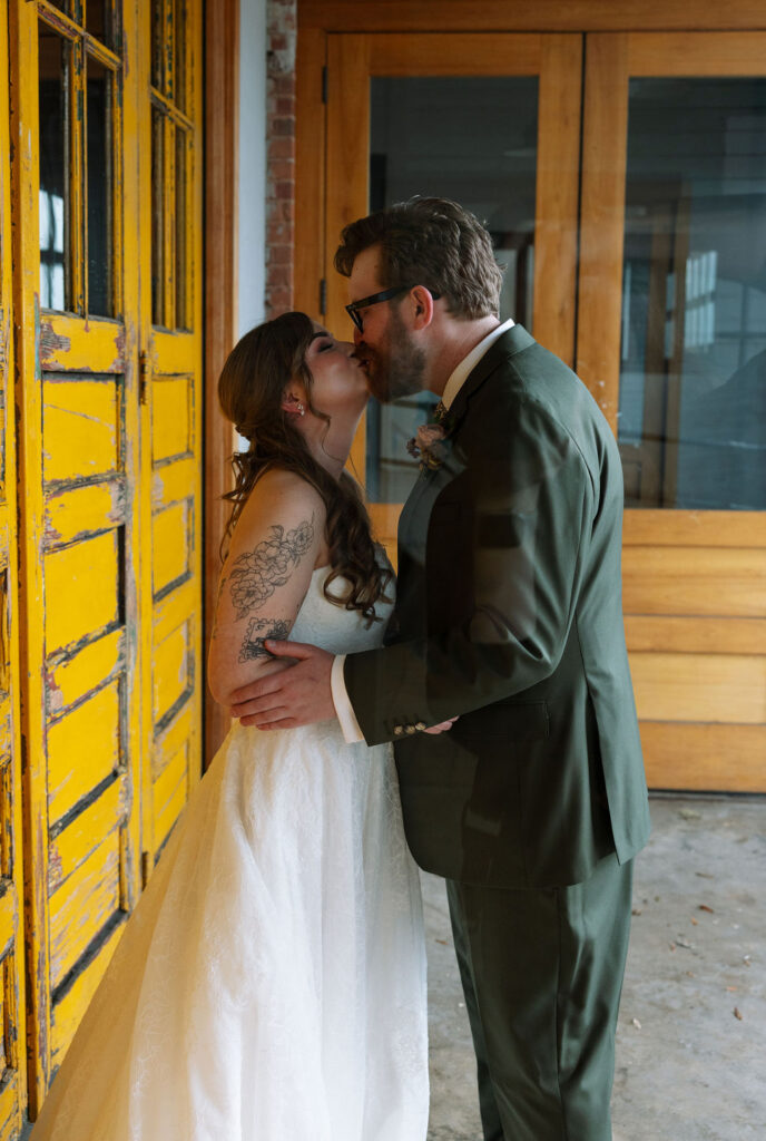 Bride and groom sharing a kiss beside a textured yellow door, photographed by a wedding photographer in Knoxville