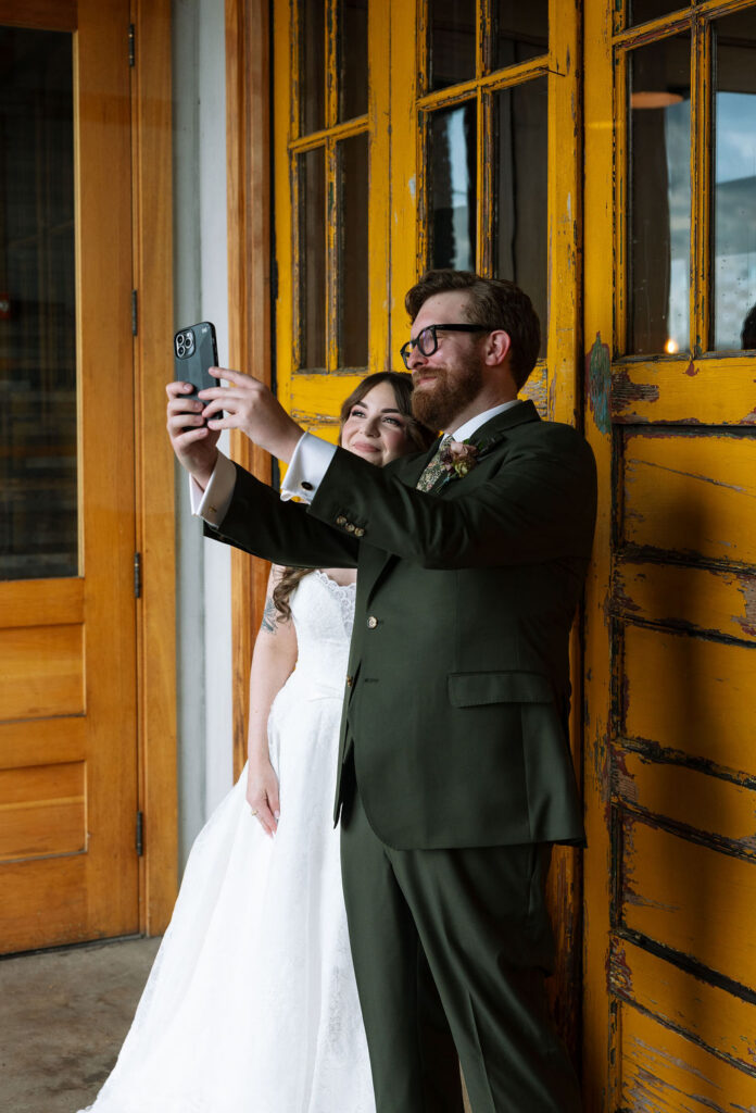 Bride and groom taking a selfie together in front of a distressed yellow door