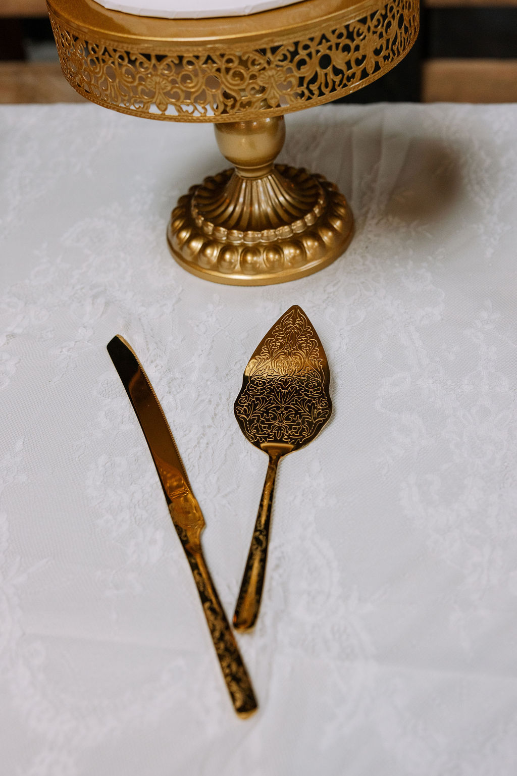 Gold cake stand with matching vintage-style cake server and knife on a lace tablecloth