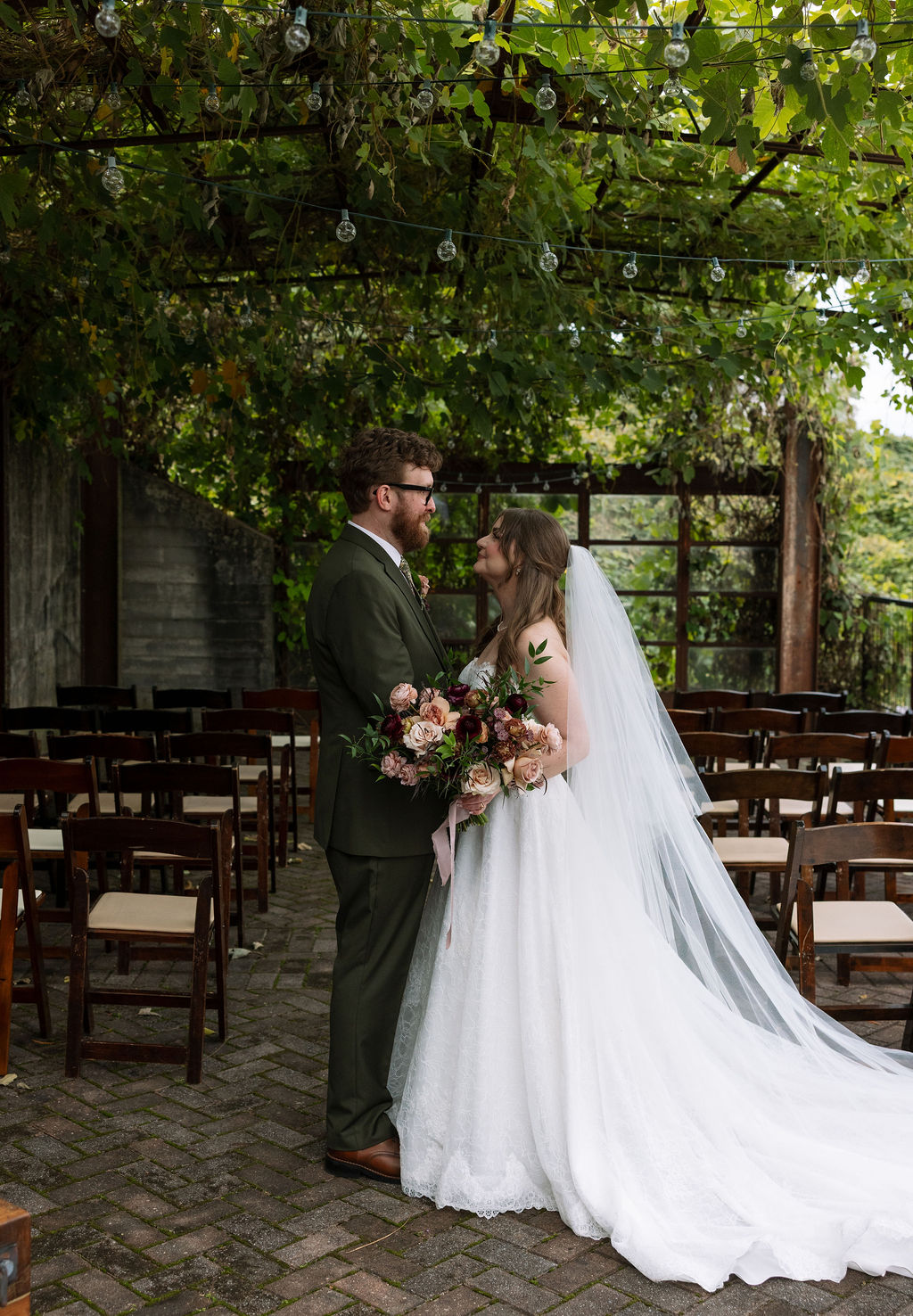 Bride and groom standing together in an outdoor ceremony space under string lights and greenery