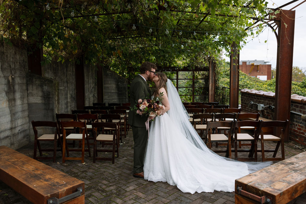 Bride and groom sharing a kiss in an outdoor ceremony space with greenery, captured by a wedding photographer in Knoxville