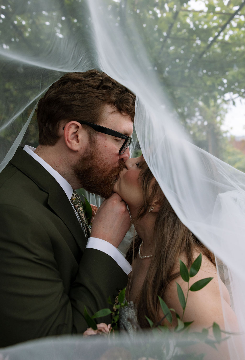 Close-up of bride and groom kissing under a soft veil with natural light filtering through