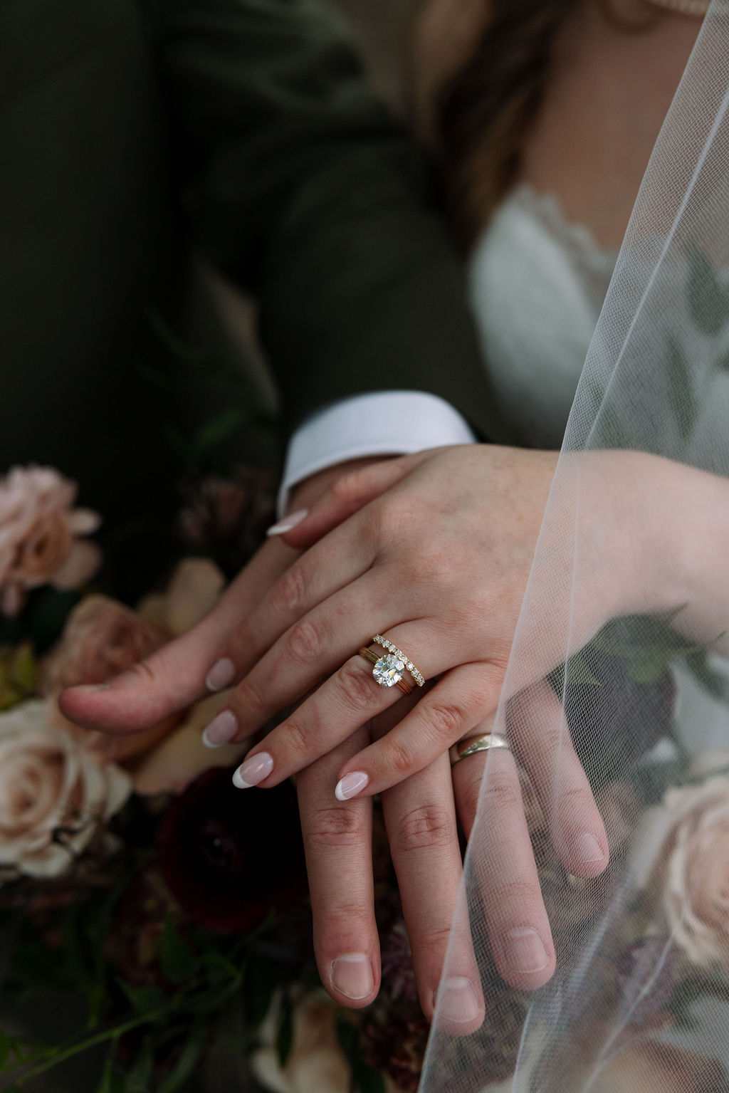 Close-up of bride and groom’s hands showing wedding rings over a soft, textured bouquet