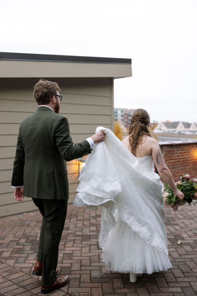 Bride and groom walking away together as the groom holds the train of her dress, photographed by a wedding photographer in Knoxville