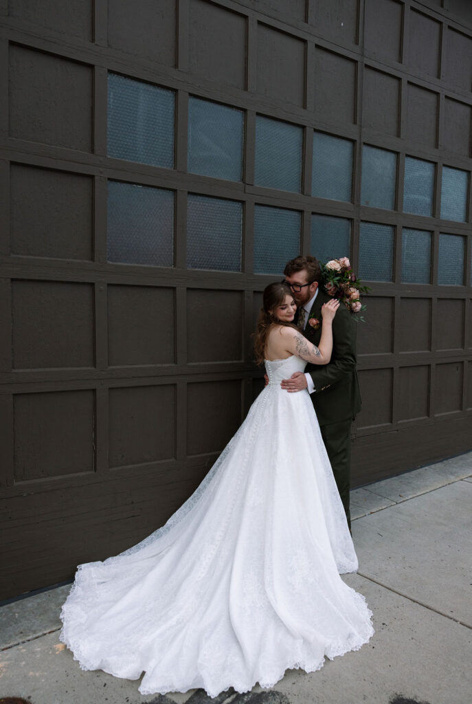 Bride and groom embracing in front of a dark paneled wall with soft, natural movement