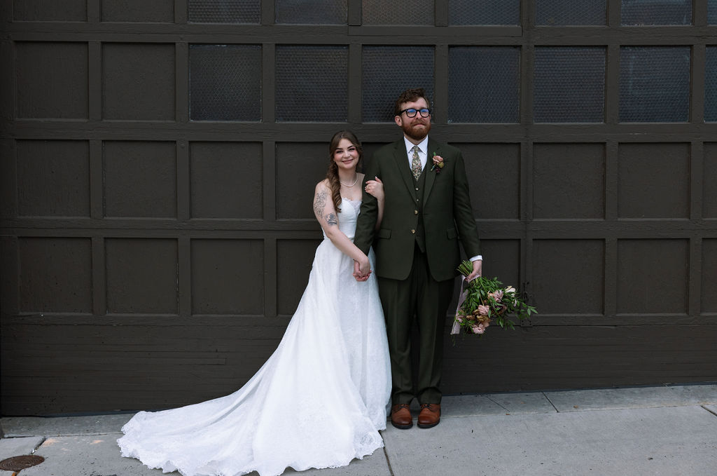 Bride and groom standing together against a dark paneled wall with relaxed, natural posture