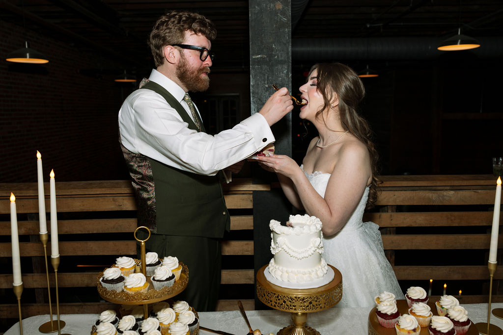 Bride and groom cutting and sharing cake surrounded by candles and desserts