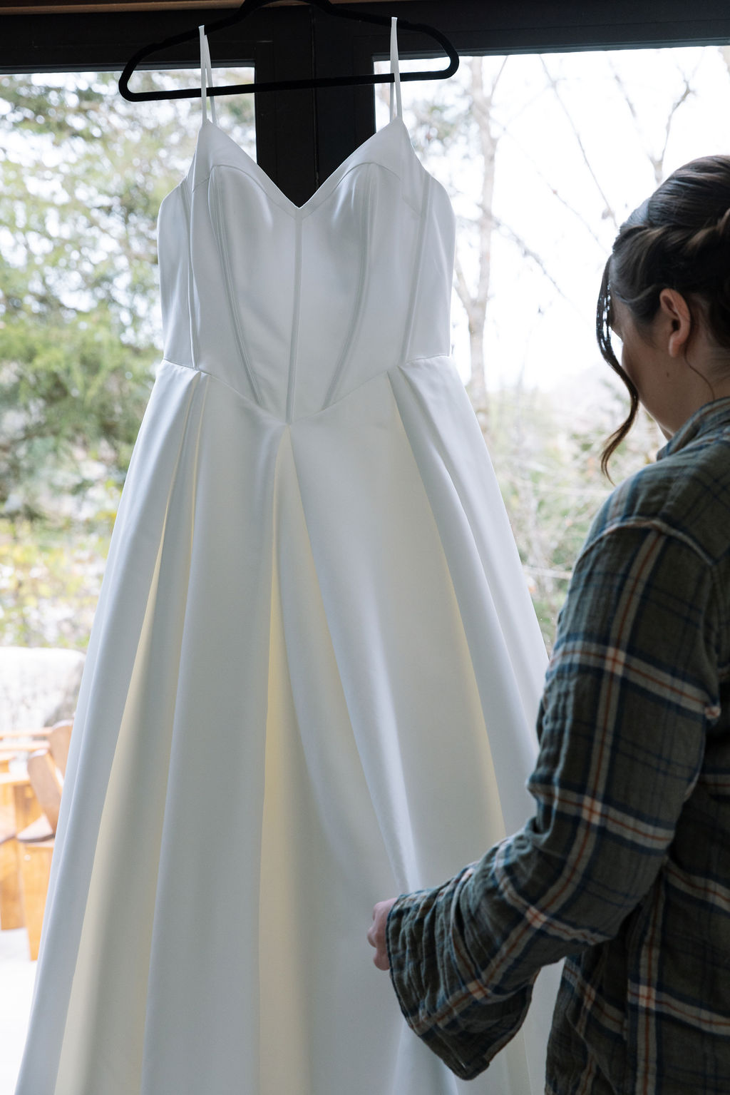Bride admiring wedding dress hanging in window light before ceremony candid wedding photography