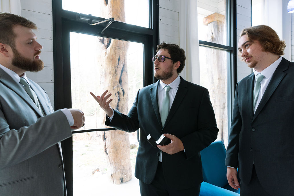 Groom talking with groomsmen by window during relaxed wedding morning preparation