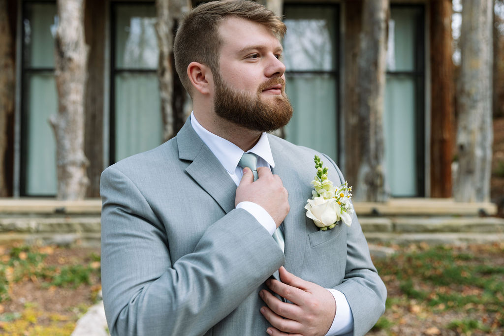 Portrait of groom adjusting tie outside rustic venue before ceremony in Tennessee