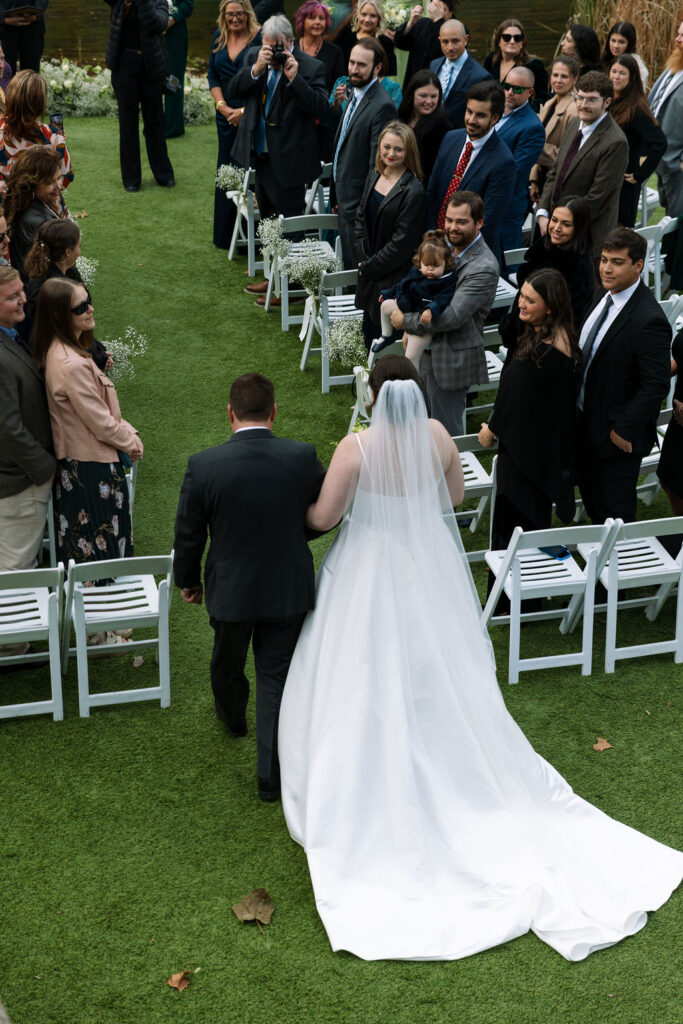 Bride walking down aisle with father surrounded by guests during candid wedding photography