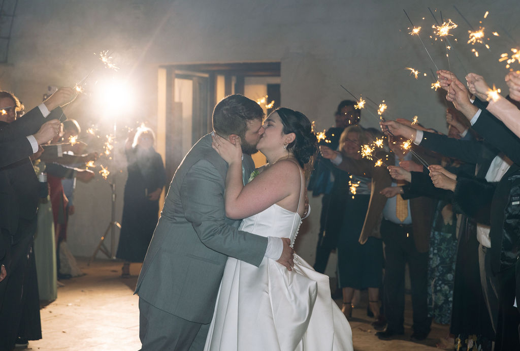 Bride and groom kissing during sparkler exit surrounded by guests captured with candid wedding photography