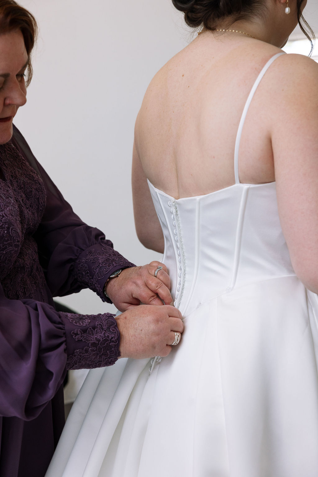 Mother fastening buttons on bride’s wedding dress during candid wedding photography getting ready moment