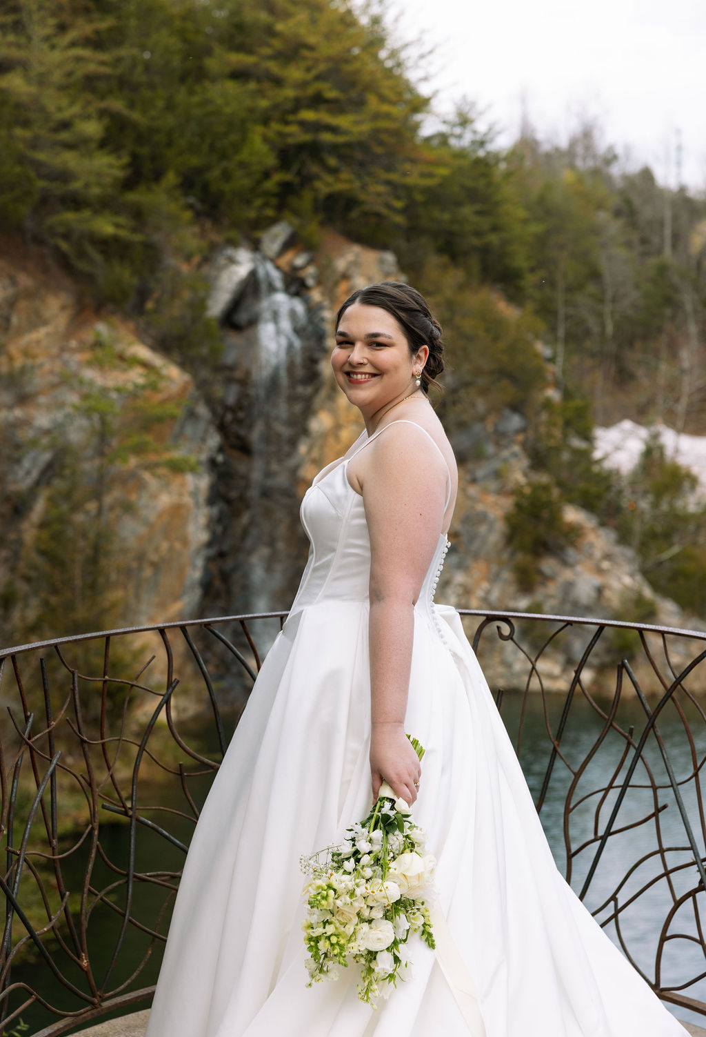 Bride smiling on balcony with waterfall backdrop captured with candid wedding photography style