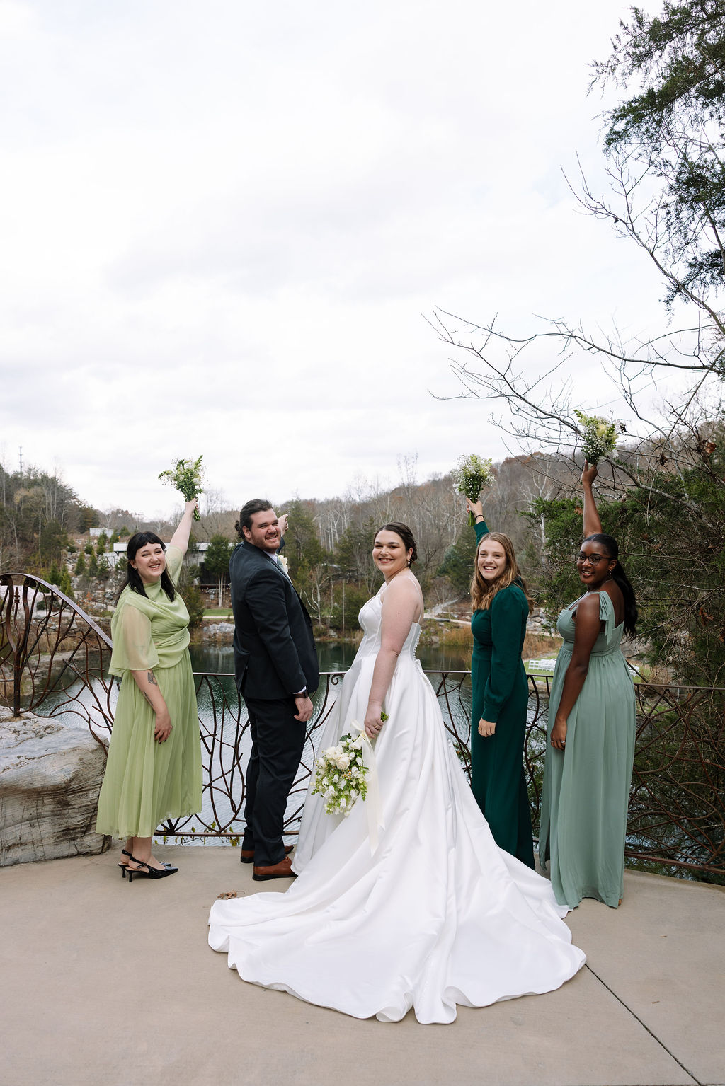 Bride and wedding party celebrating on overlook with waterfall backdrop during candid wedding photography