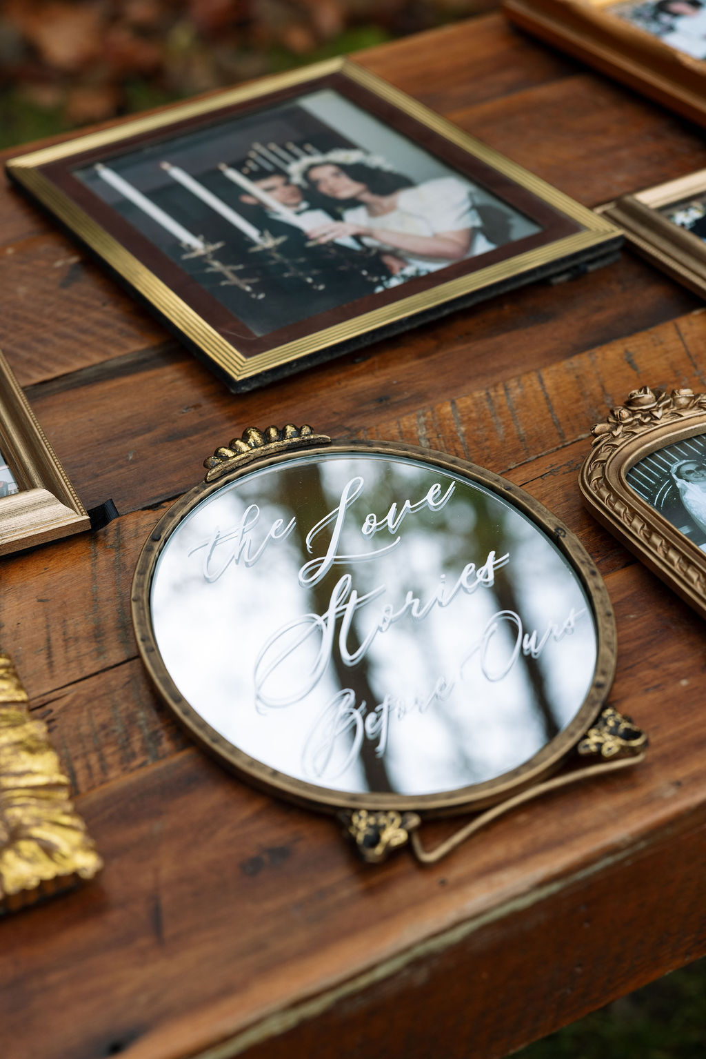 Framed family wedding photos and mirror sign displayed on wooden table during wedding reception details