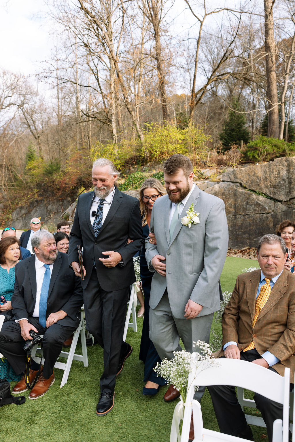 Groom walking down aisle with family during outdoor ceremony candid wedding photography moment