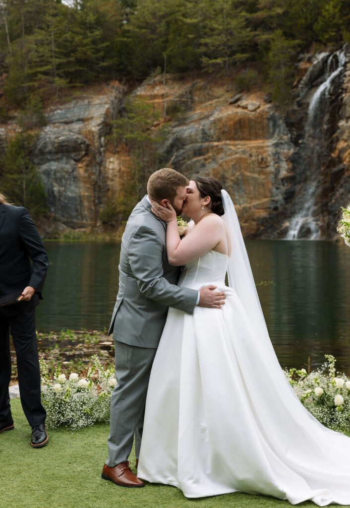 Bride and groom sharing first kiss during outdoor waterfall ceremony candid wedding photography