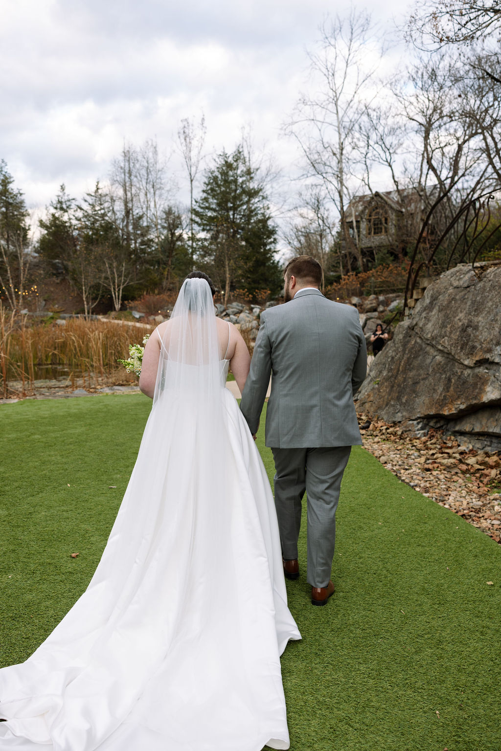 Newly married couple walking together after ceremony beside waterfall captured with candid wedding photography