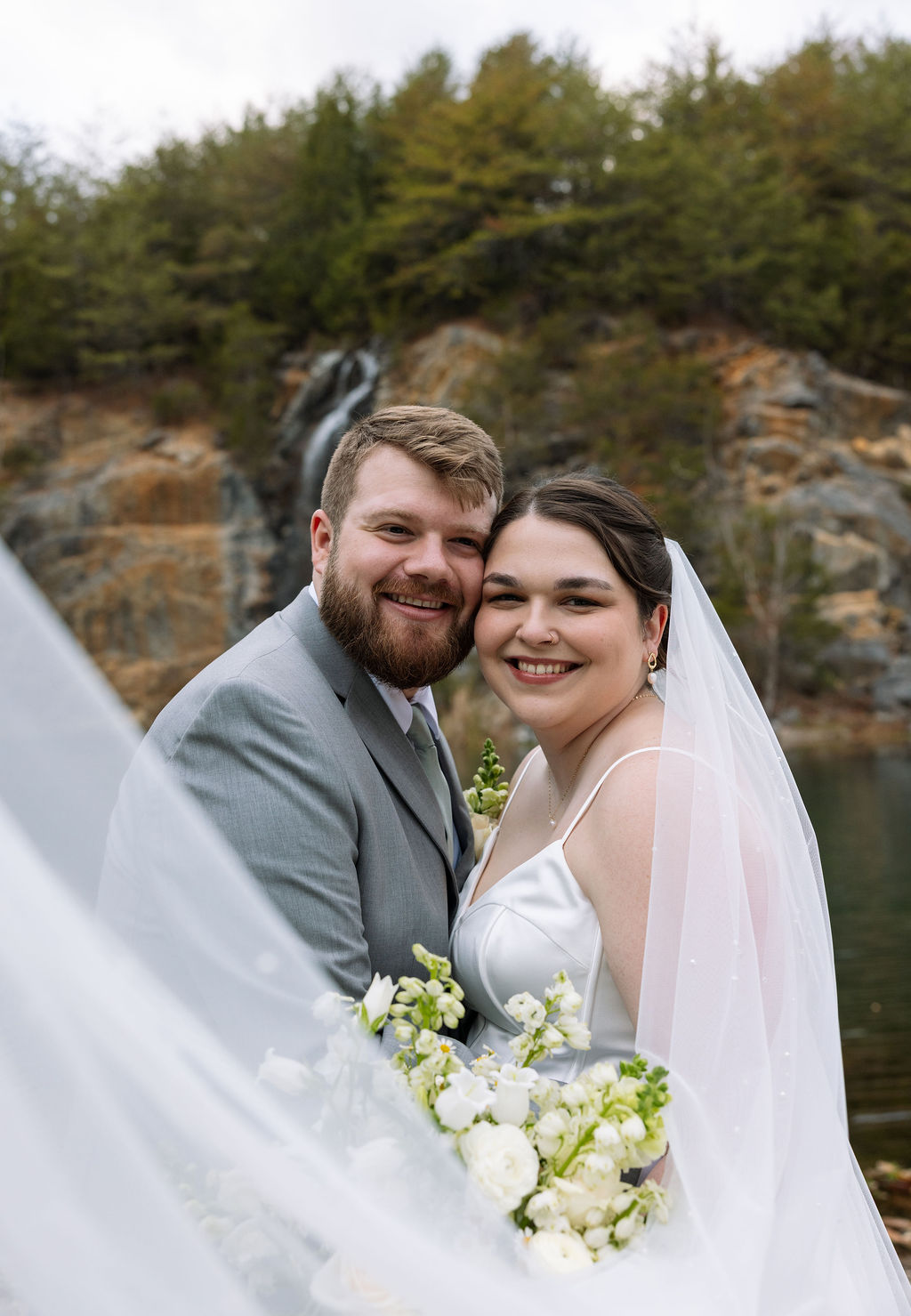 Close portrait of bride and groom smiling together with veil and waterfall backdrop