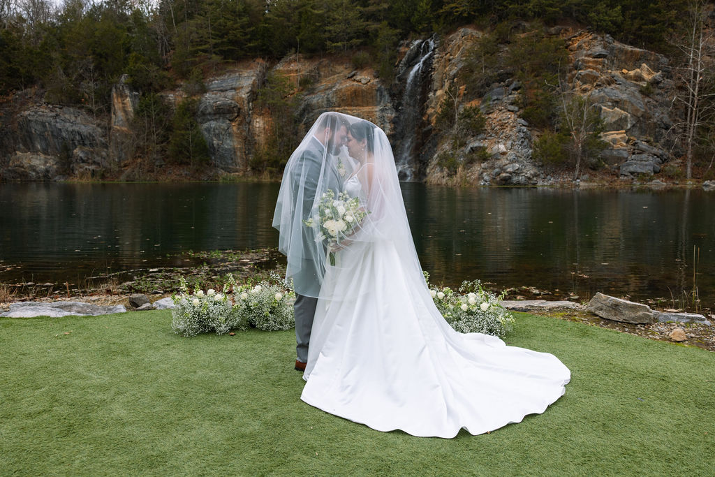 Bride and groom sharing quiet veil moment beside waterfall captured with candid wedding photography