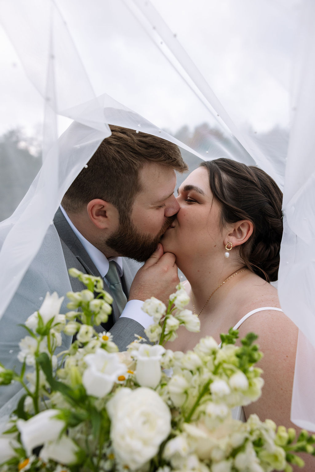 Bride and groom kissing under veil surrounded by flowers captured with candid wedding photography