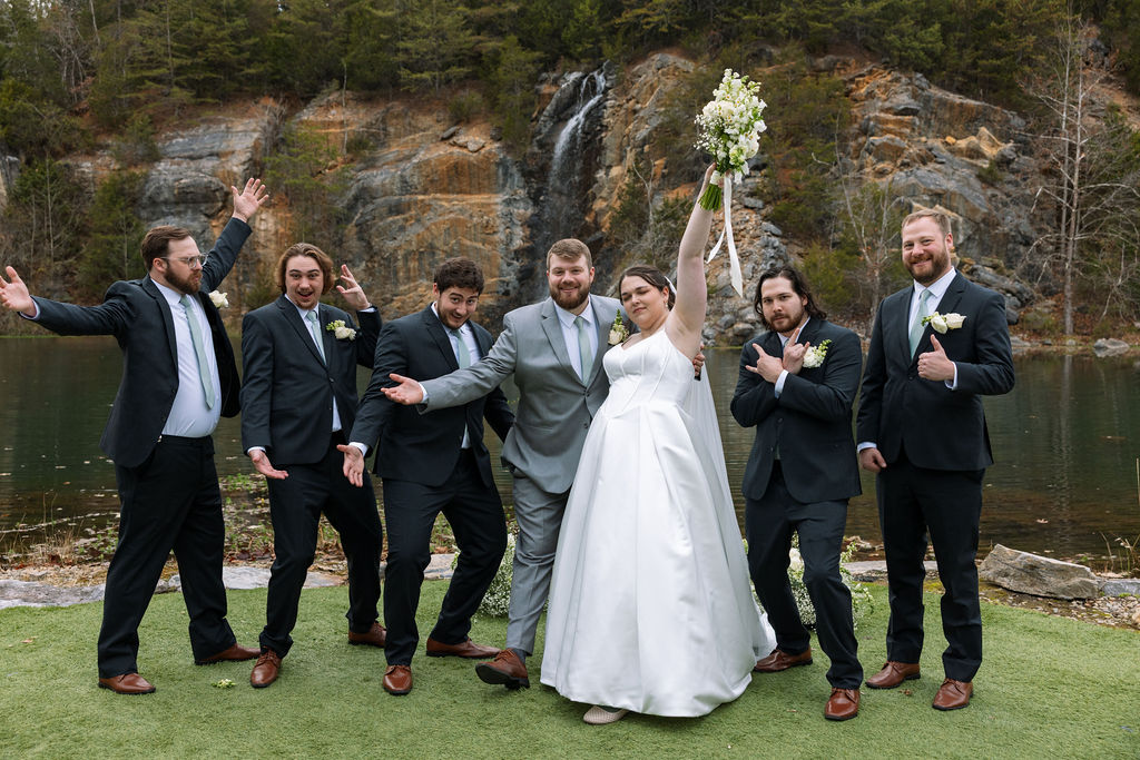 Bride celebrating with groomsmen during candid wedding photography portraits by Tennessee waterfall