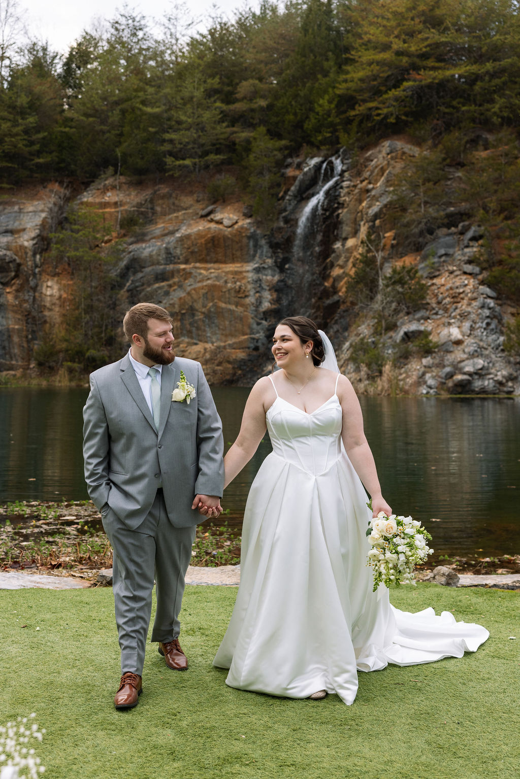 Bride and groom walking hand in hand by waterfall captured with candid wedding photography style