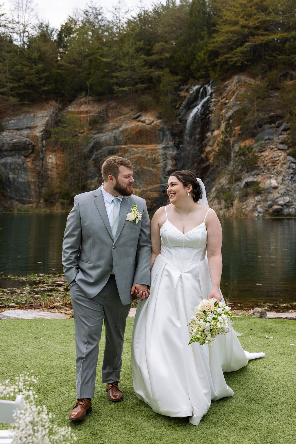 Bride and groom walking beside waterfall during candid wedding photography portrait at Tennessee wedding venue