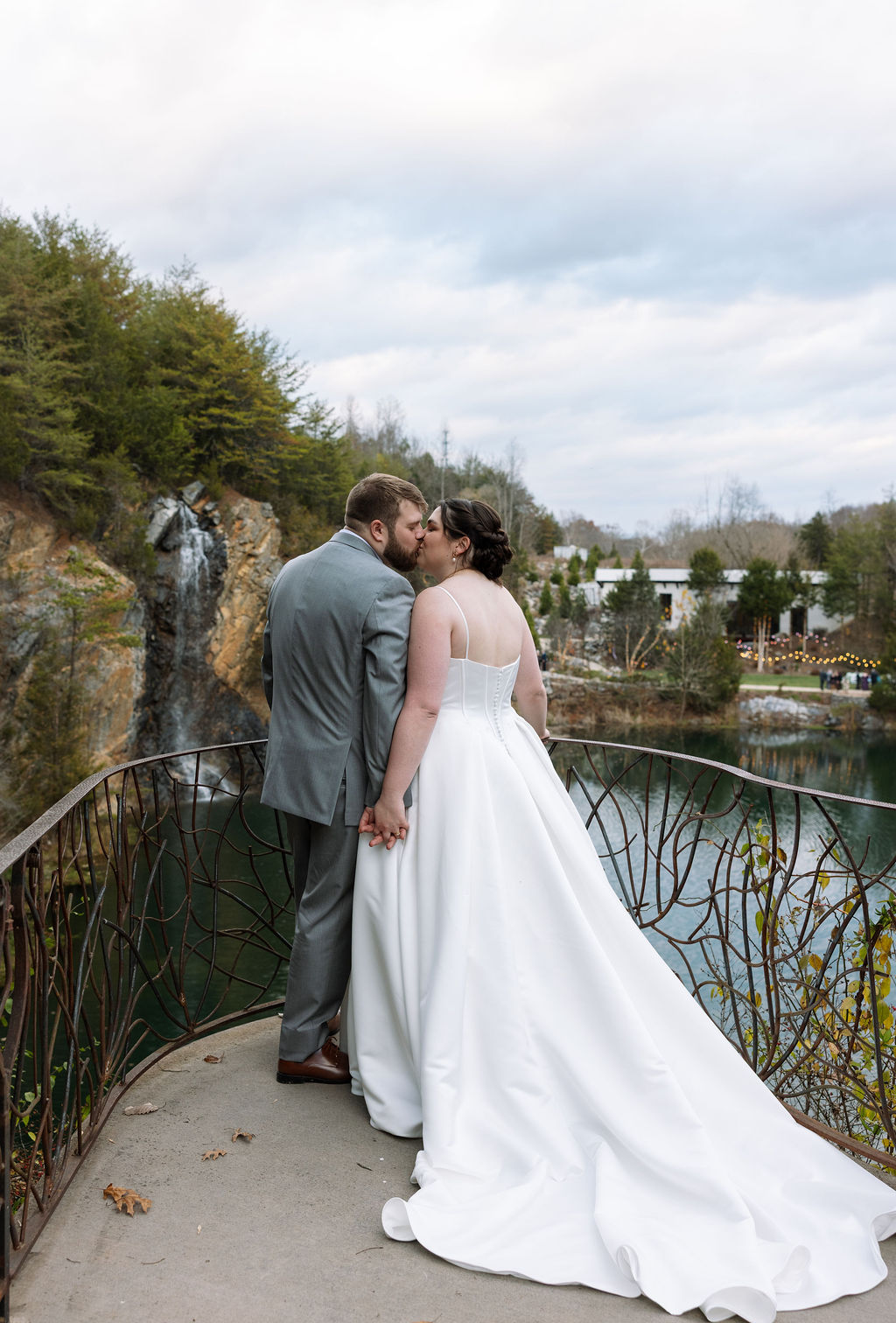 Bride and groom kissing on overlook above waterfall captured in candid wedding photography