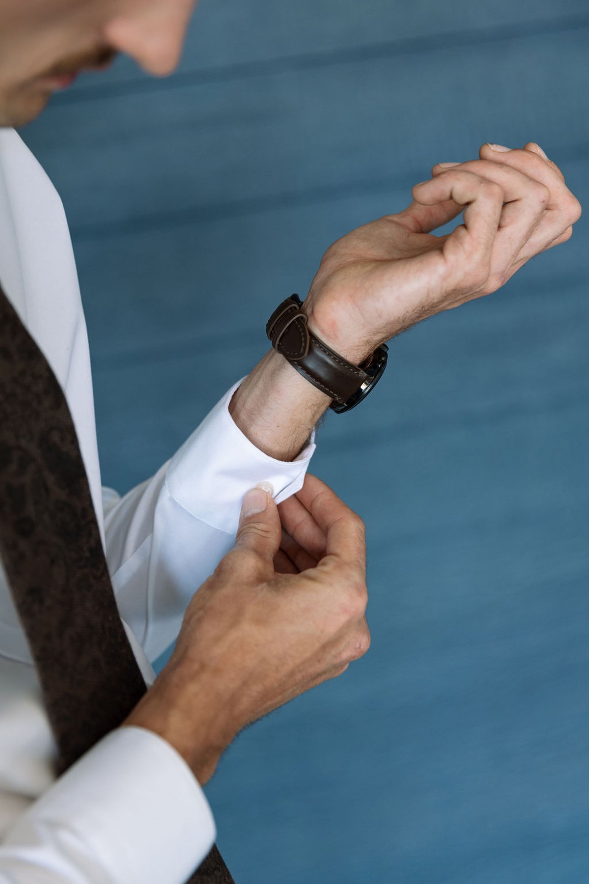 Groom adjusting cufflinks and watch during wedding morning preparations