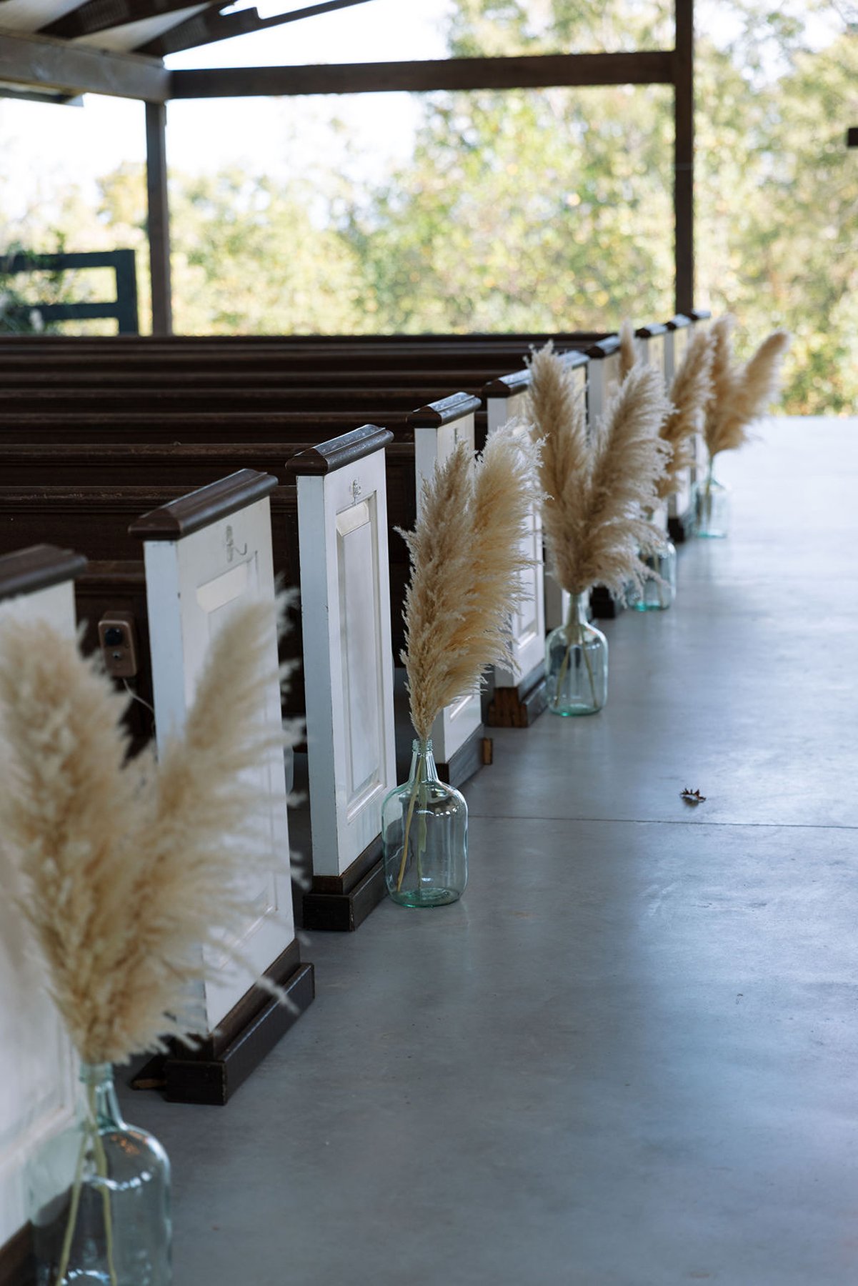 Aisle lined with pampas grass arrangements in glass vases at ceremony space
