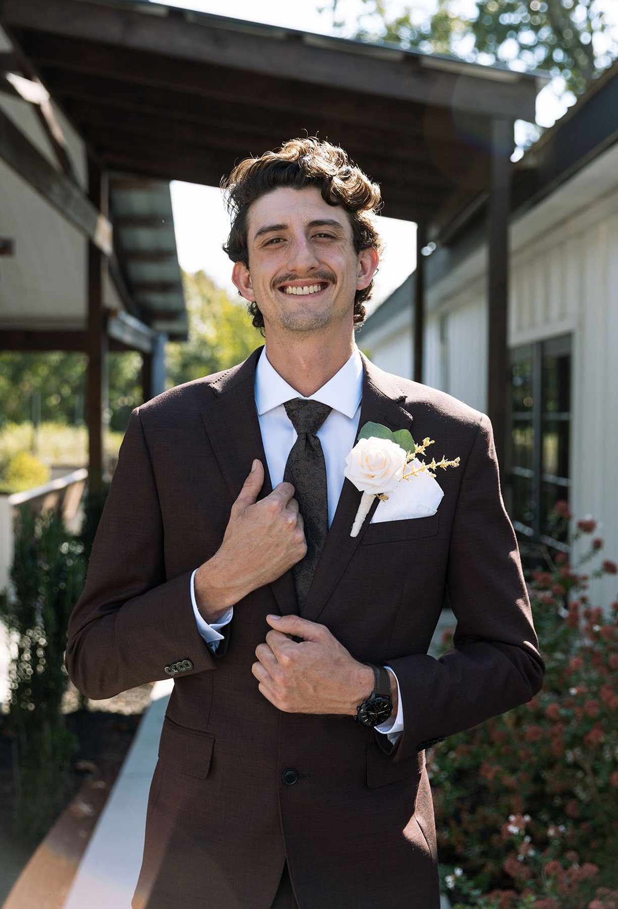 Groom portrait adjusting tie with boutonniere in natural outdoor light