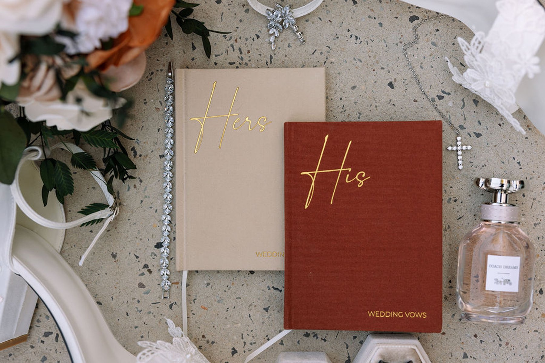 Wedding detail flat lay with vow books, jewelry, and perfume
