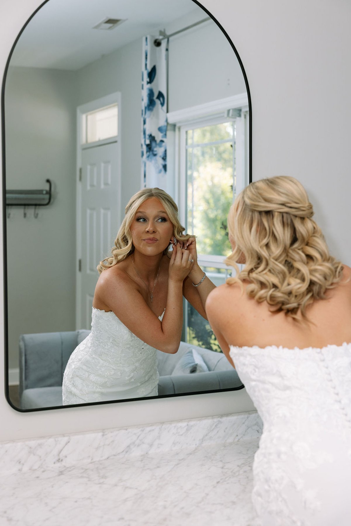 Bride putting on earrings in mirror during wedding morning preparations