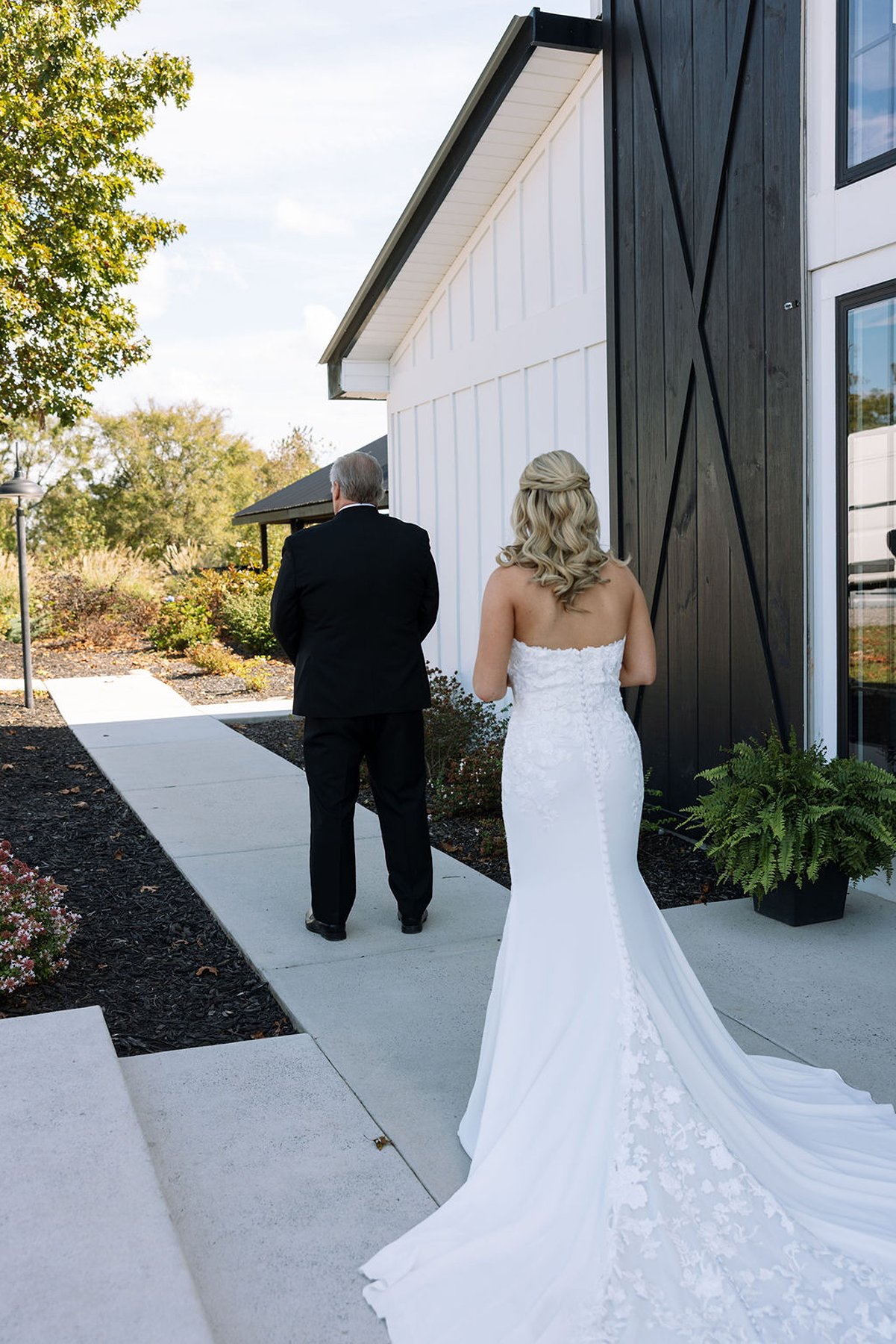 Bride approaching ceremony with father outside white barn wedding venue