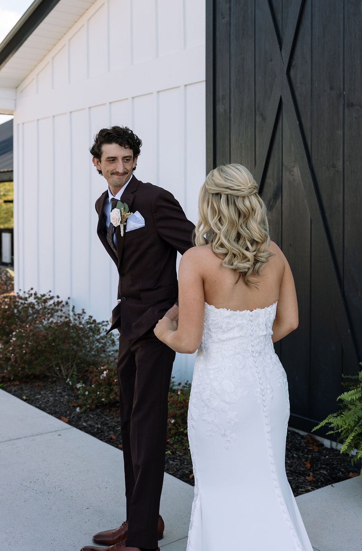Groom turning to see bride during first look outside white barn venue
