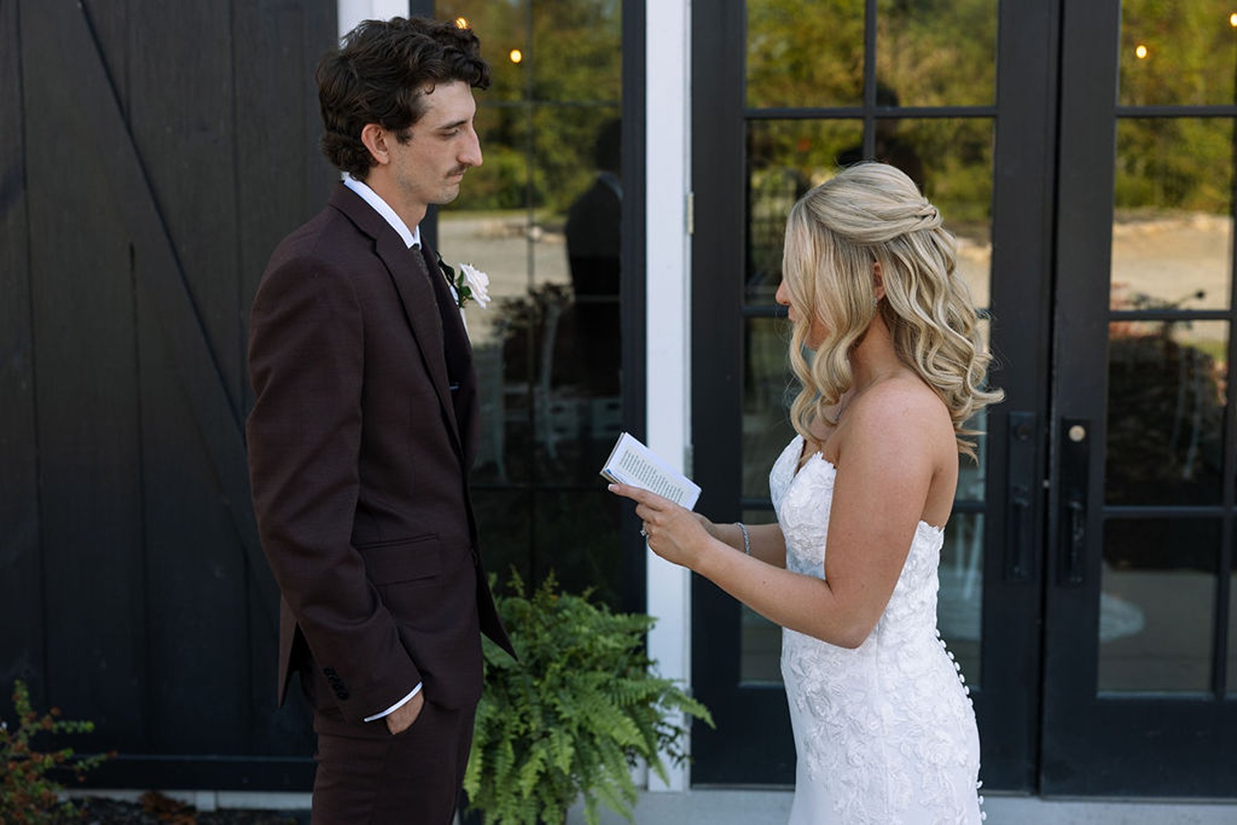 Bride reading vows to groom outside modern barn doors before ceremony
