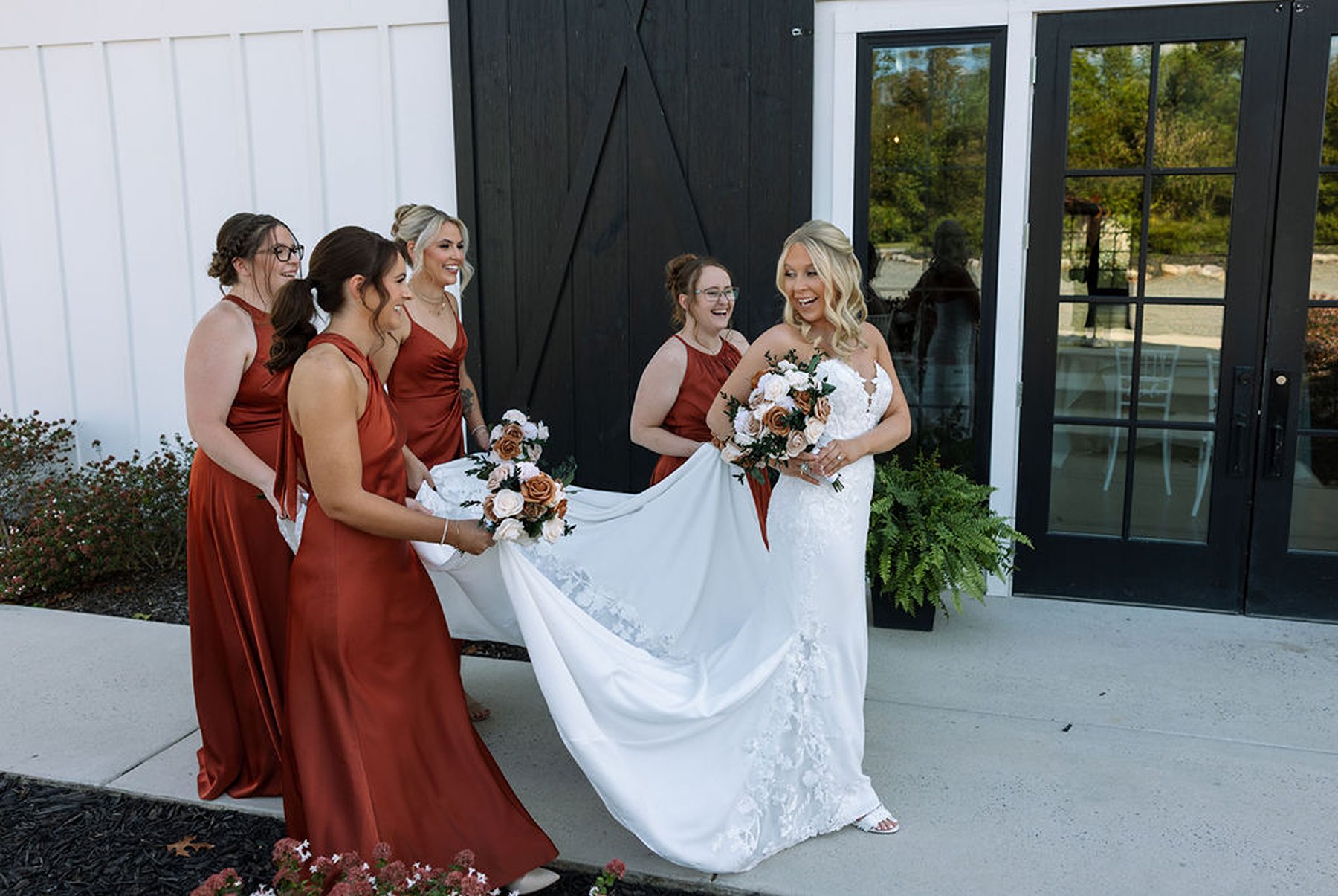 Bridesmaids helping bride with dress and laughing outside modern venue