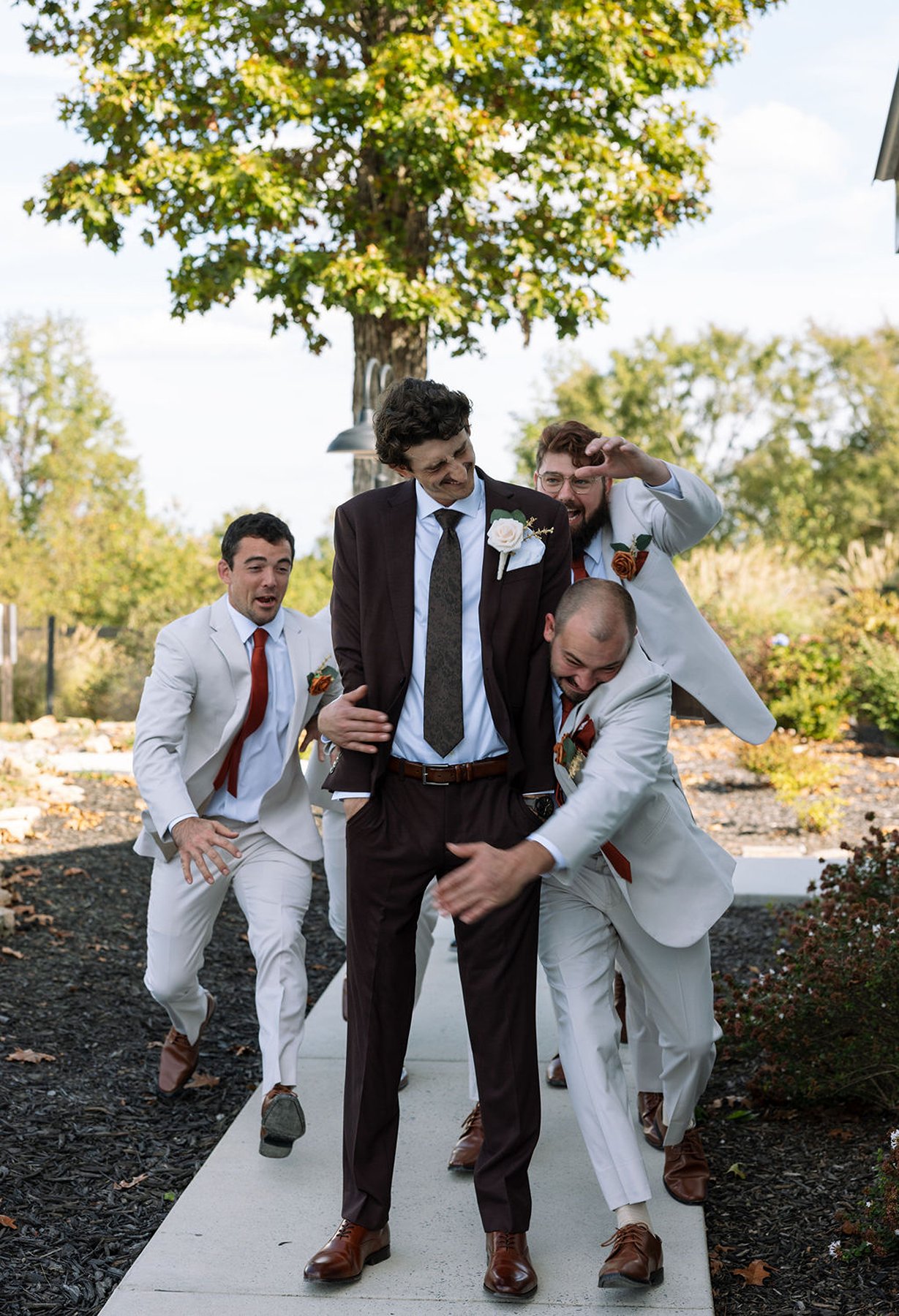 Groomsmen playfully grabbing groom during candid moment on walkway