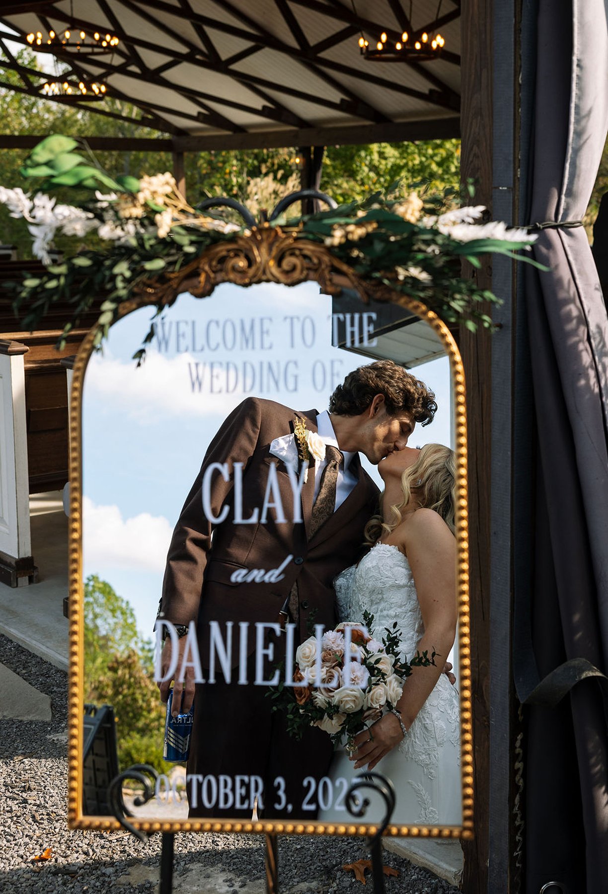 Bride and groom kissing reflected in welcome sign mirror display