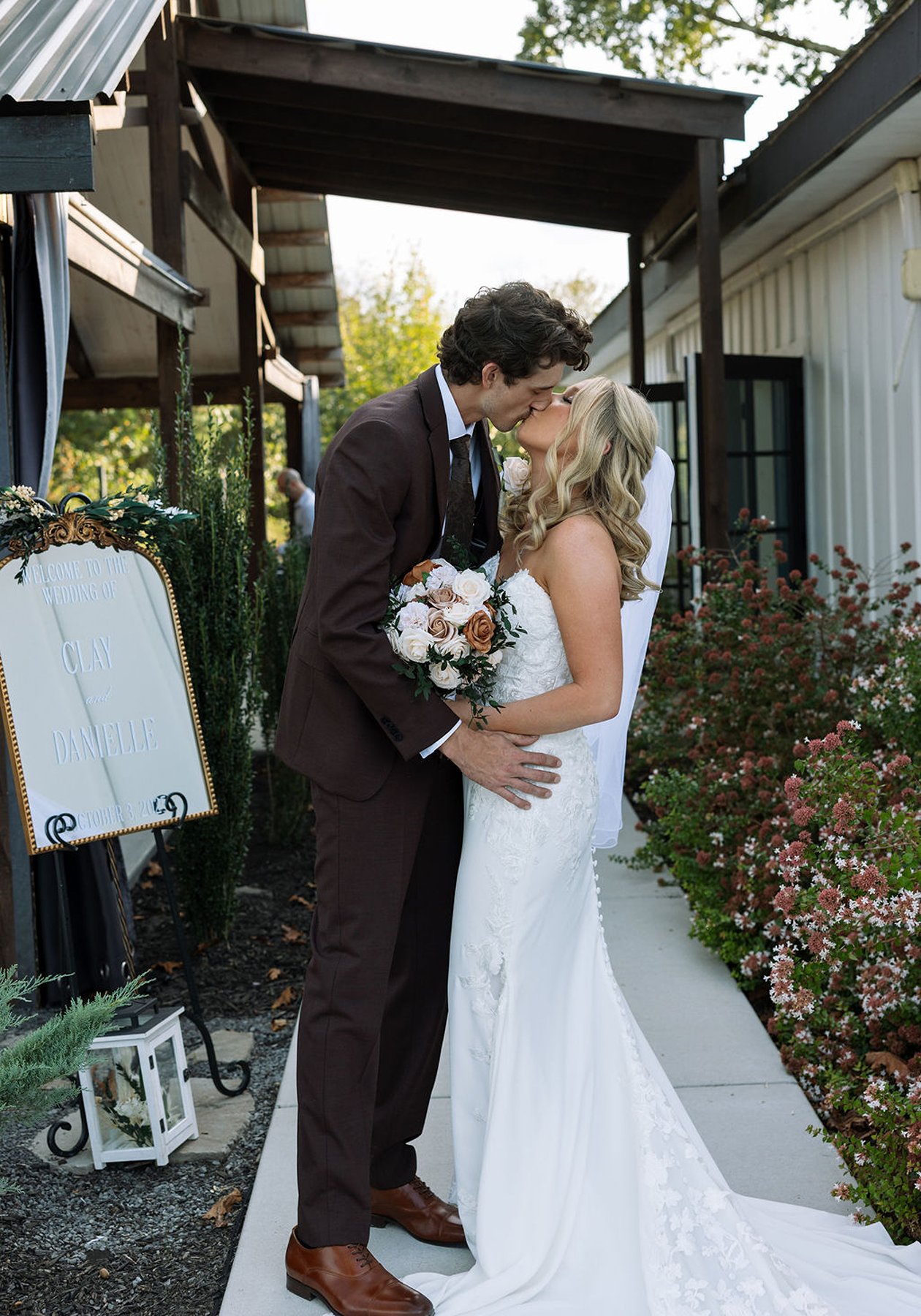 Bride and groom kissing along garden walkway with florals and signage